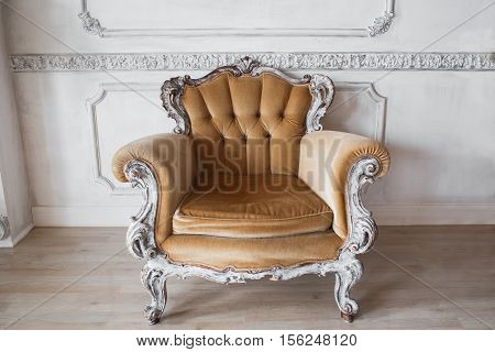 Living room with antique stylish beige armchair on luxury white wall design bas-relief stucco mouldings roccoco elements.