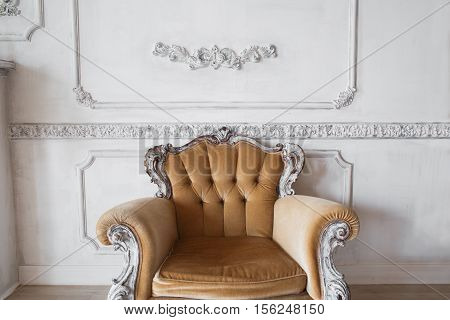 Living room with antique stylish beige armchair on luxury white wall design bas-relief stucco mouldings roccoco elements.