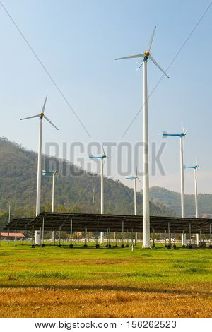 solar panels with wind turbines against mountanis landscape against blue sky