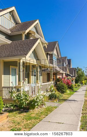 Row of houses on a sunny day with side walk and trees.