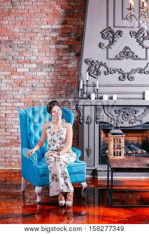 Beautiful woman with blue eyes and curly hair in dress on luxory interer background the fireplace chandelier. blue sofa.