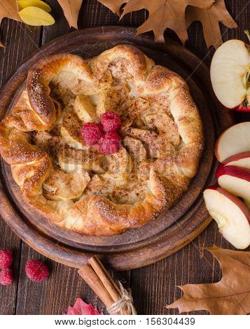 apple pie with cinnamon and raspberry on a wooden table.