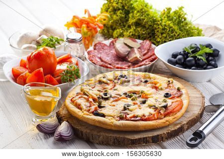 Delicious italian pizza and ingredients served on the white wooden table