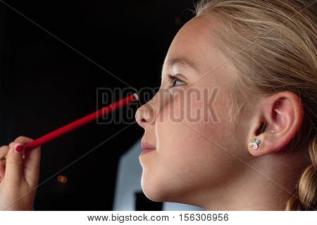 Profile portrait of a beautiful young smiling girl while she holds a pencil pointed to her eye