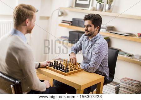 Two young men playing chess in room