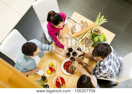 Group of happ young people sitting by the table eating and drinking red wine