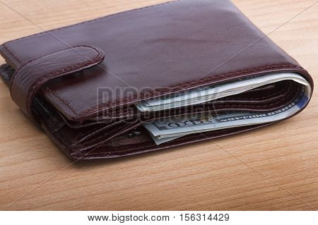 brown men's wallet with money on a wooden background