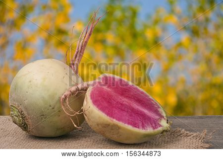 One whole and sliced watermelon radish on a wooden table with blurred garden background.