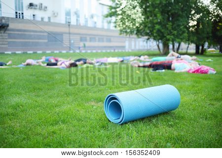 People do yoga training in park near building at summer day, focus on mat