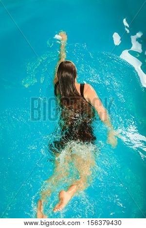 Woman resting at swimming pool. Young girl wearing black dress floating. Water aerobics fitness.