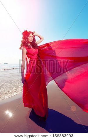 Beautiful girl in a bright red dress by the sea. Against the background of the summer lanshaft. Young romantic woman in the sunshine, sunset.