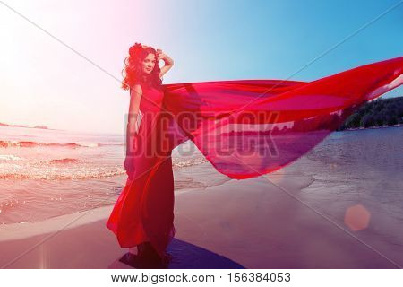 Beautiful girl in a bright red dress by the sea. Against the background of the summer lanshaft. Young romantic woman in the sunshine, sunset.
