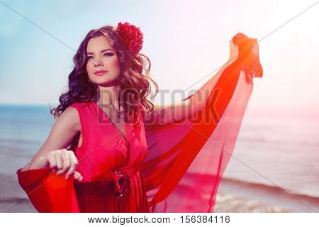 Beautiful girl in a bright red dress by the sea. Against the background of the summer lanshaft. Young romantic woman in the sunshine, sunset.