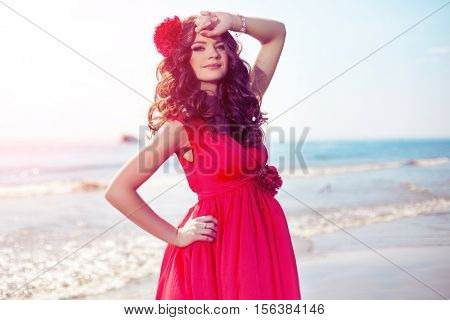 Beautiful girl in a bright red dress by the sea. Against the background of the summer lanshaft. Young romantic woman in the sunshine, sunset.