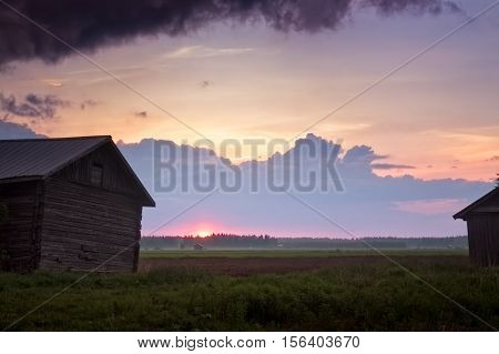 The summer sun sets between the old barn houses in the Northern Finland. The fields are still cold in June and the mist rises when the air is getting cooler.