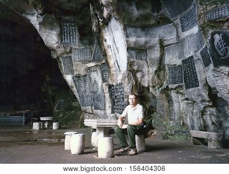 GUILIN, CHINA / CIRCA 1987: An American traveler sits on a bench inside the ancient Thousand Buddha Cave.