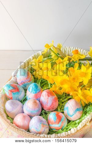 Close Up of Basket of Hand Painted Easter Eggs with Daffodils on Table Vertical with Copy Space