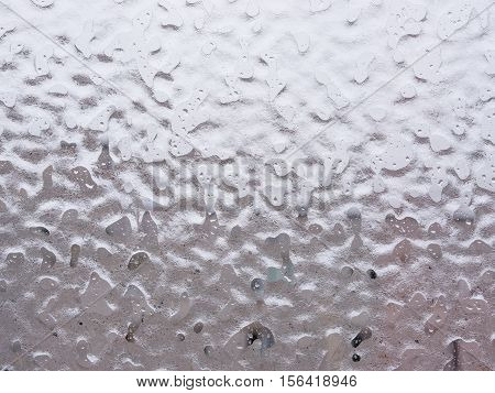 Texture of ice and drops on window glass in inclement winter weather. Close up. Icy rain background