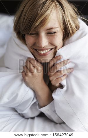 Blond woman snuggled up in duvet nice and cozy