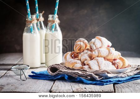 Rugelach with jam filling on plate with milk on wooden background