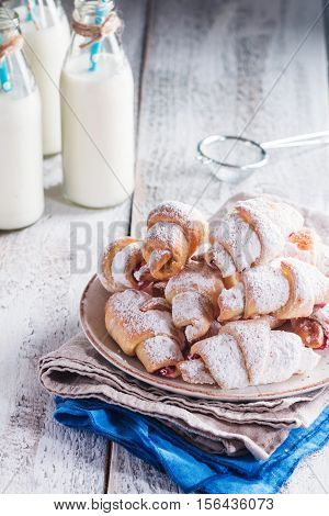 Rugelach with jam filling on plate with milk on wooden background