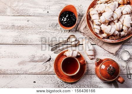 Rugelach with jam filling on plate with tea on white wooden background, top view with copy space