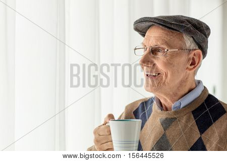 Elderly man holding a cup and looking through a window