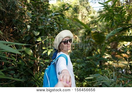 Follow me. Travel concept. Back view of young woman with backpack outdoors discovering jungle holding boyfriend's hand.