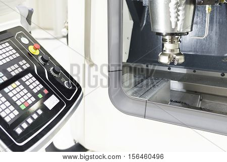 The face milling tool with the raw material work piece on the CNC milling machine in the silver tone effect and the controller panel