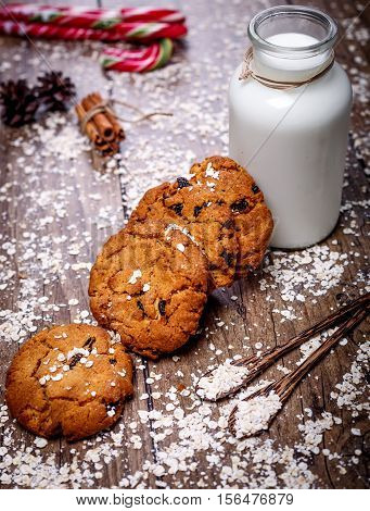 Homemade oatmeal cookies with nuts and raisins and glass of milk on dark wooden background