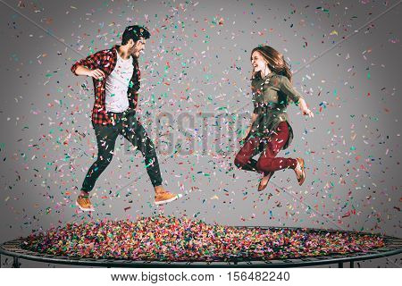 Mid-air fun. Mid-air shot of beautiful young cheerful couple jumping on trampoline together with confetti all around them