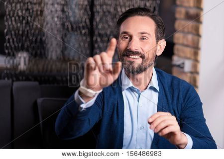 Positive entertainment. Happy optimistic nice man smiling and pressing his finger to the virtual screen while having fun in virtual reality