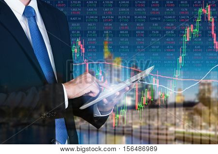 Businessman using digital tablet working with stock market chart in computer screen over the stock market exchange on frankfurt cityscape in background Business trading and technology concept.