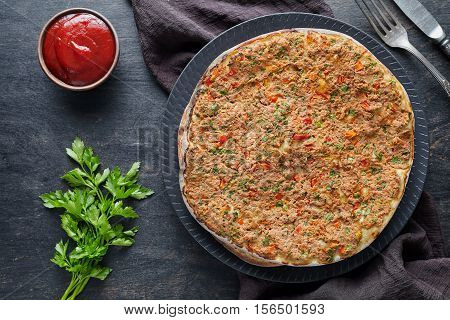 Lahmacun traditional turkish gourmet pizza with minced beef or lamb meat, paprika, tomatoes, cumin spice, parsley baked spicy middle eastern food on dark table background
