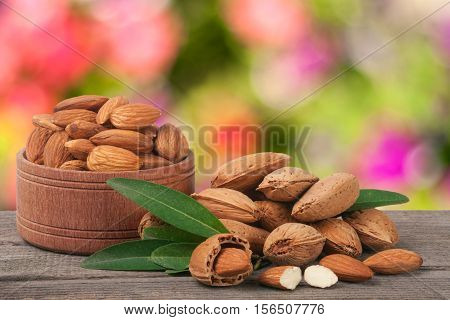 almonds in a bowl on the old wooden board with blurred garden background.