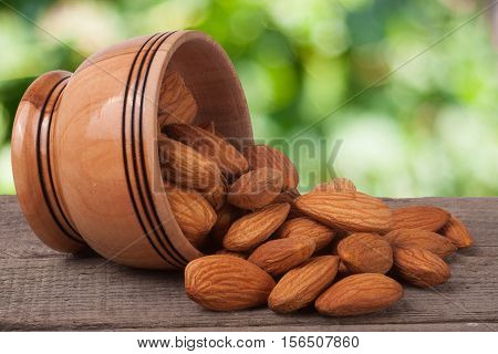 almonds in a bowl on the old wooden board with blurred garden background.