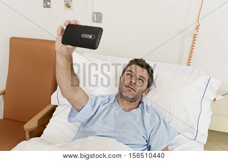 young sad man lying on bed hospital clinic holding mobile phone taking self portrait selfie photo in pesimist recovery concept feeling wasted and depressed