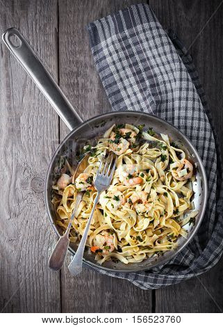 Tagliatelle with shrimps on the pan placed on a wooden table