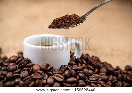 White coffeecup on coffeebeans with spoon above on gunny background