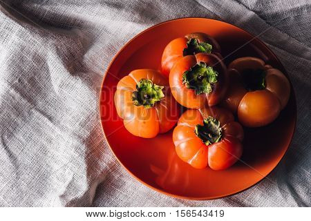 Some Persimmons on Orange Plate. High Angle View