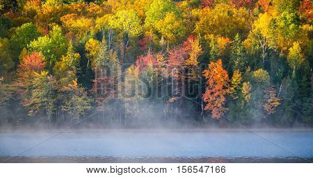 Vibrant October colors on autumn deciduous trees reflected on calm water of Corry Lake.