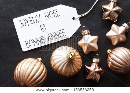Label With French Text Joyeux Noel Et Bonne Annee Means Merry Christmas And Happy New Year. Bronze Christmas Tree Balls On Black Paper Background. Christmas Decoration Or Texture. Flat Lay View