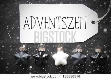 Label With German Text Adventszeit Means Advent Seasons. Black And White Christmas Tree Balls On Black Paper Background With Snowflakes. Christmas Decoration Or Texture. Flat Lay View