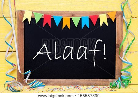 Blackboard With German Text Alaaf Means Happy Carnival. Party Decoration Like Streamer And Confetti. Yellow Wooden Background. Greeting Card For Celebrations