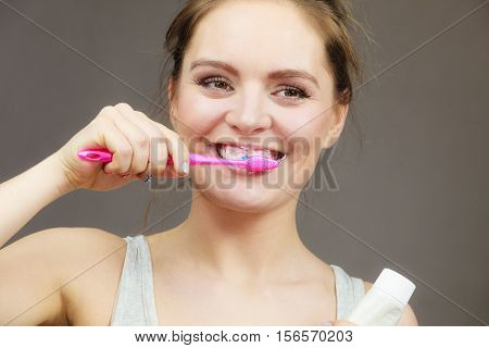 Woman holding brush and tooth paste for teeth cleaning. Happy funny smiling girl with toothbrush. Oral hygiene. Studio shot dark background