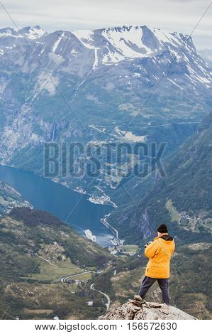 Tourism vacation and travel. Male tourist taking photo with camera enjoying Geiranger fjord and mountains landscape from Dalsnibba Plateau viewpoint Norway Scandinavia.