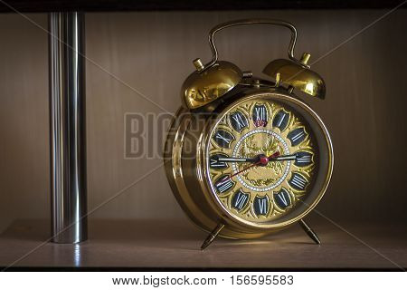 An old clock standing on a shelf of modern furniture.