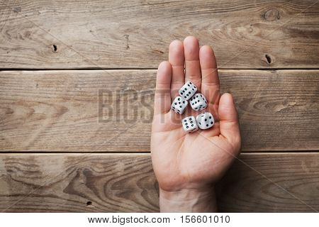 Man holding in hand white dice over the wooden table from above. Gambling devices. Game of chance concept.