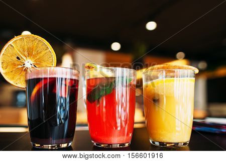 Colorful punch drinks on bar, close-up. Three glasses with fruit sangria, blurred restaurant background, free space. Refreshment, party, menu, relax, friendship, diversity concept