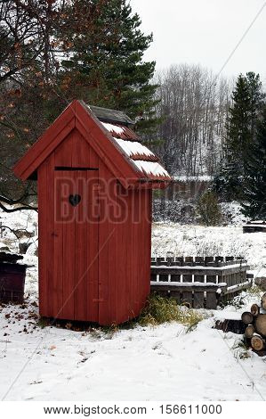 A Red wooden outhouse toilet on wintertime.